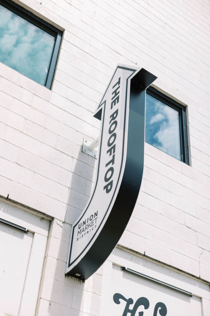 Black and white arrow sign labeled 'The Rooftop, Union Market District' on a brick wall, guiding guests to rooftop event space