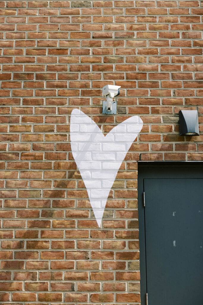 White heart outline painted around a security camera on a red brick wall near Union Market rooftop entrance