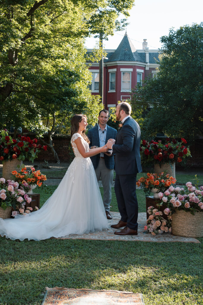 Couple exchanging vows during a garden ceremony at The Branch Museum in Richmond, Virginia, surrounded by lush florals and historic architecture.