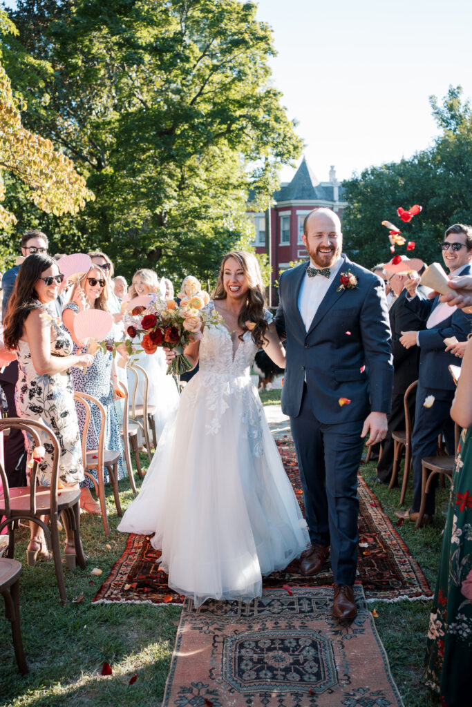 Joyful wedding recessional at The Branch Museum, with guests tossing petals as the newlyweds walk down a vintage rug-lined aisle.