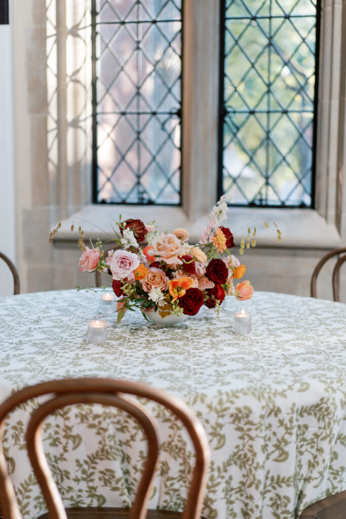 Garden-inspired floral centerpiece with coral, blush, and garnet blooms on a patterned green-and-white linen at The Branch Museum wedding reception.