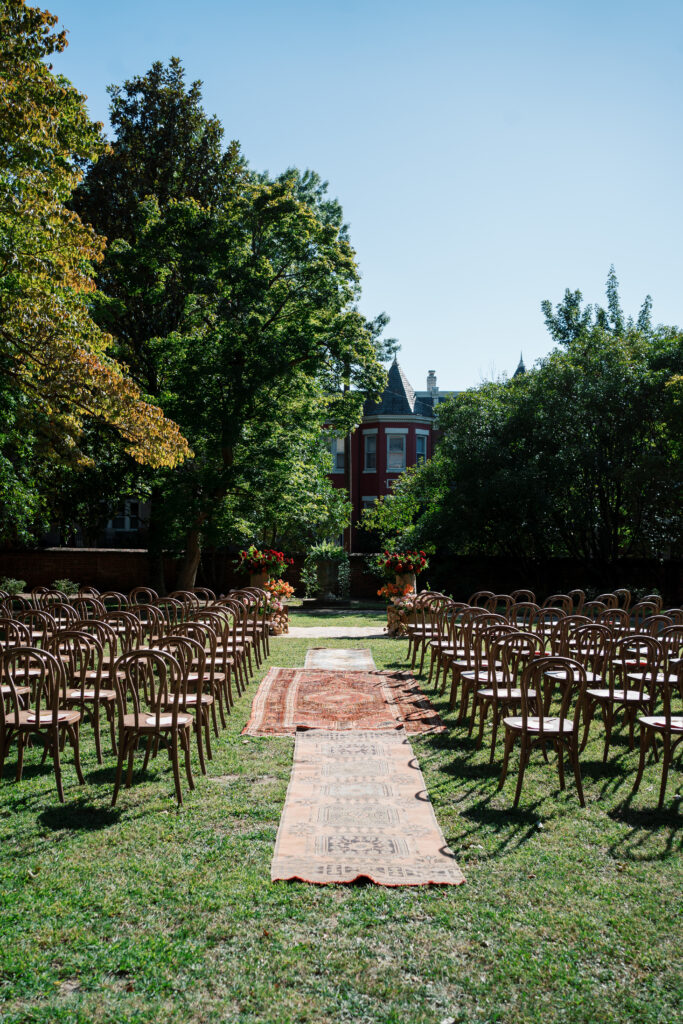 Vintage rug aisle runner, wooden ceremony chairs for an outdoor wedding ceremony in the garden at The Branch Museum in Richmond, Virginia