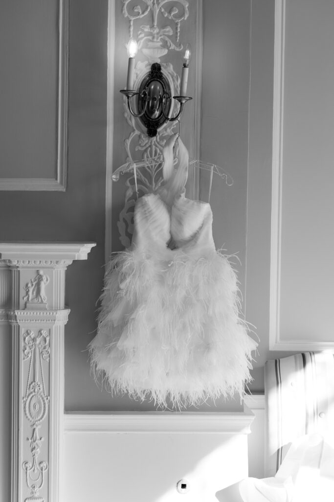 Feathered mini wedding reception dress hanging in historic Richmond venue, styled with vintage wall sconces Second Look Wedding Dress.