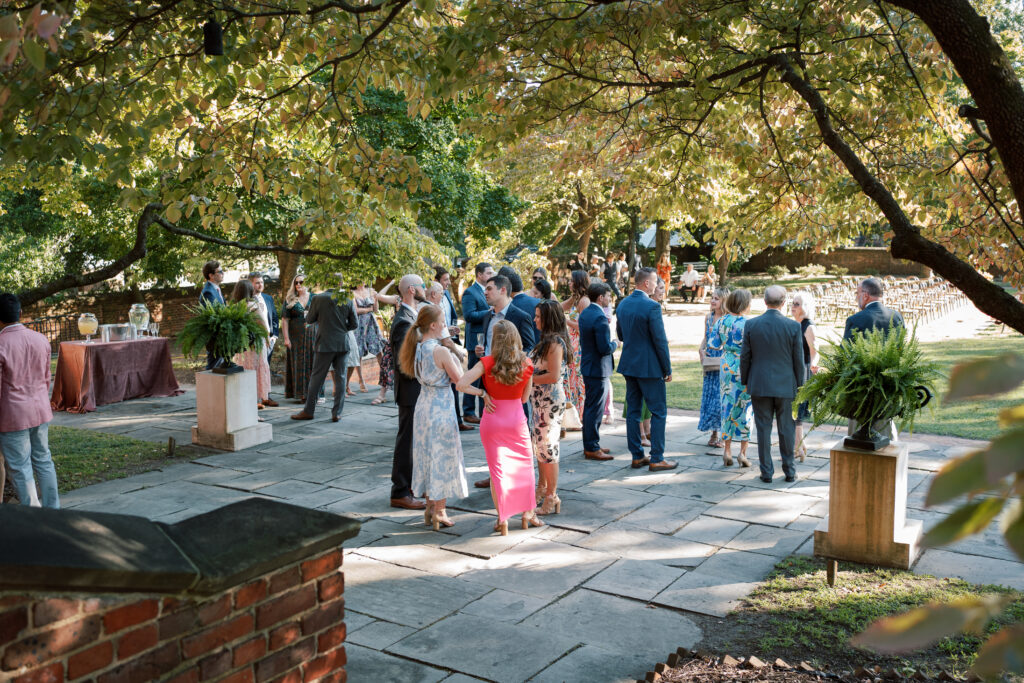 Guests mingling during cocktail hour beneath the trees in the garden courtyard at The Branch Museum in Richmond, Virginia. Richmond Va Wedding.