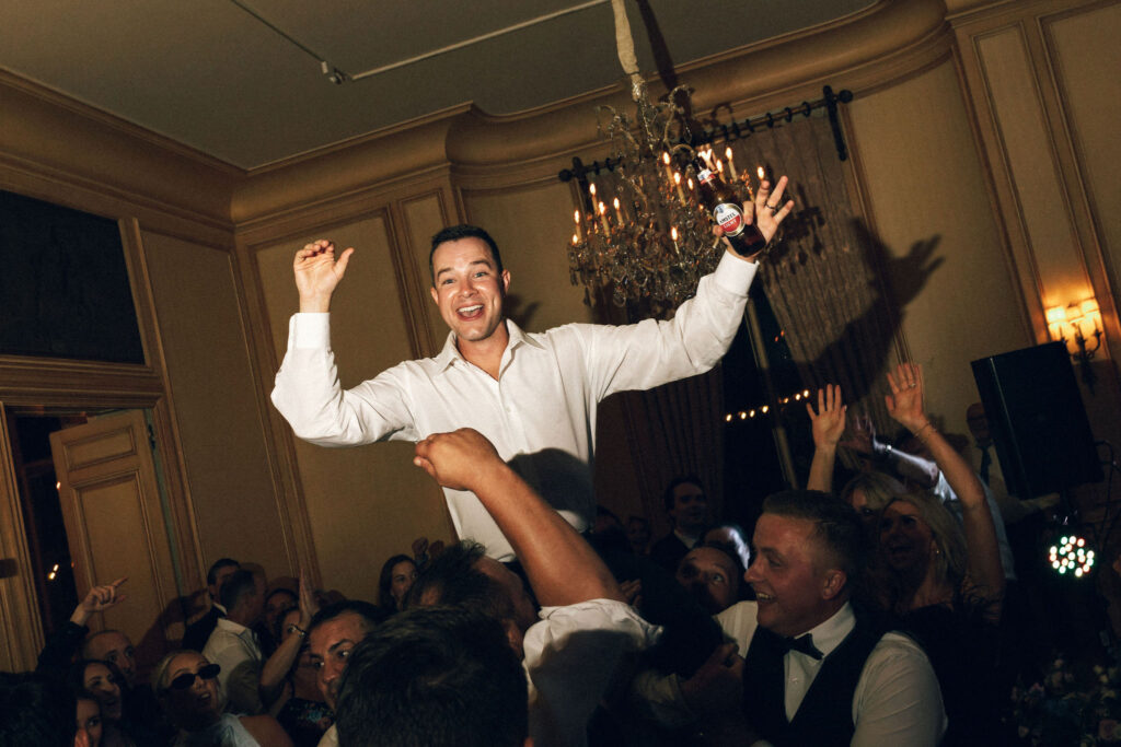 Groom lifted into the air by a cheering crowd under a chandelier during the Meridian House wedding reception.
