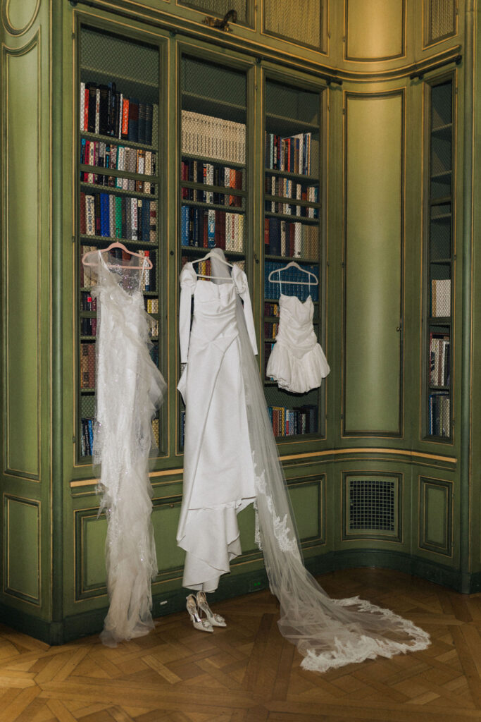Three bridal gowns worn by the bride during her wedding at Meridian House in Washington, D.C., displayed in the historic library with green built-in bookshelves.