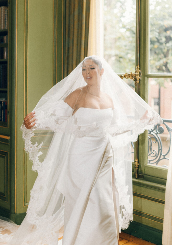 Editorial bridal portrait with bride wrapped in a dramatic lace veil inside the Meridian House library before the ceremony.