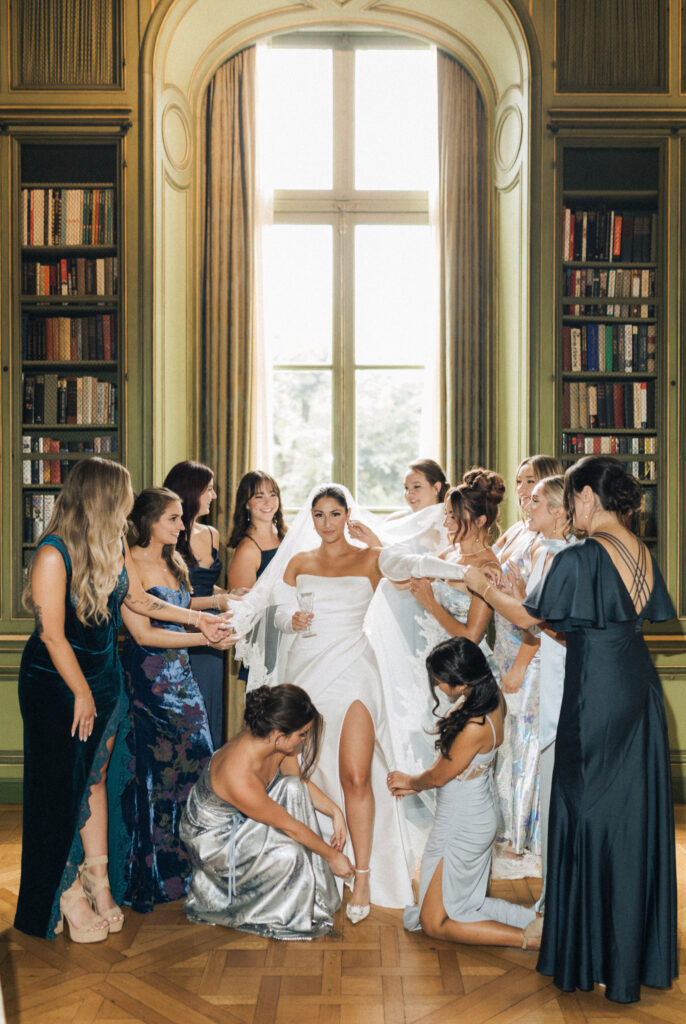 Bridal party helping the bride get ready in the Meridian House library, adjusting her gown and veil before the ceremony. Blue, fashion forward mismatched, bridesmaids dresses.