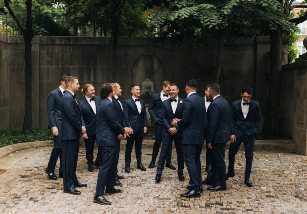 Groom laughing with groomsmen in tuxedos in the Meridian House courtyard and gardens before the ceremony.