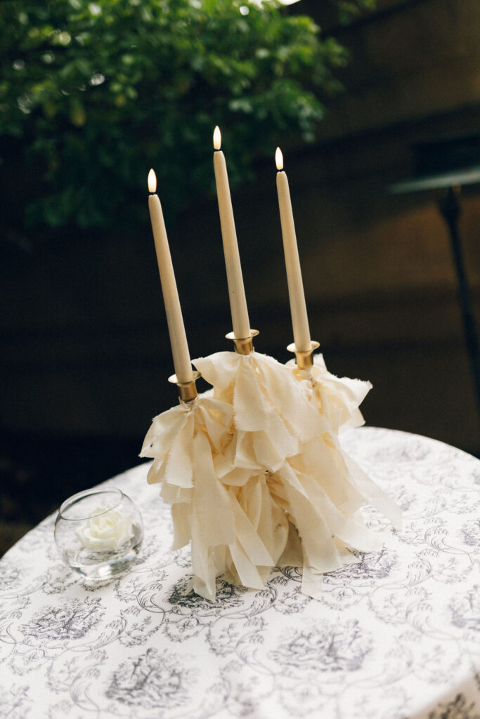 Three taper candles with ivory ribbon detailing on a toile-covered cocktail table at Meridian House in Washington, D.C.