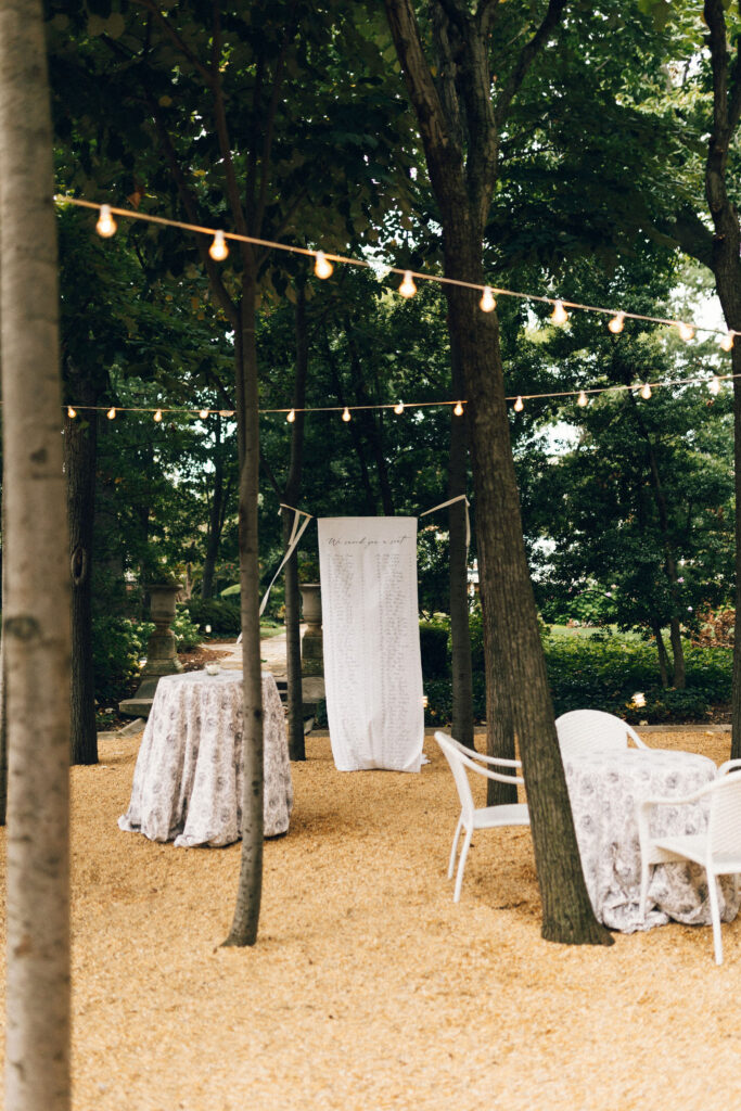 Outdoor seating area at Meridian House with bistro lights and a custom fabric seating chart hanging between trees.