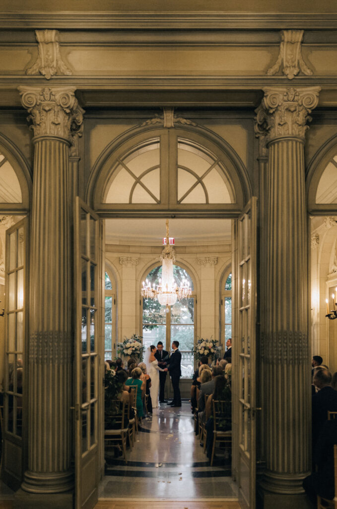 Bride and groom celebrate their wedding ceremony with guests at Meridian House in Washington, D.C., surrounded by elegant floral arrangements and natural light pouring through arched windows.