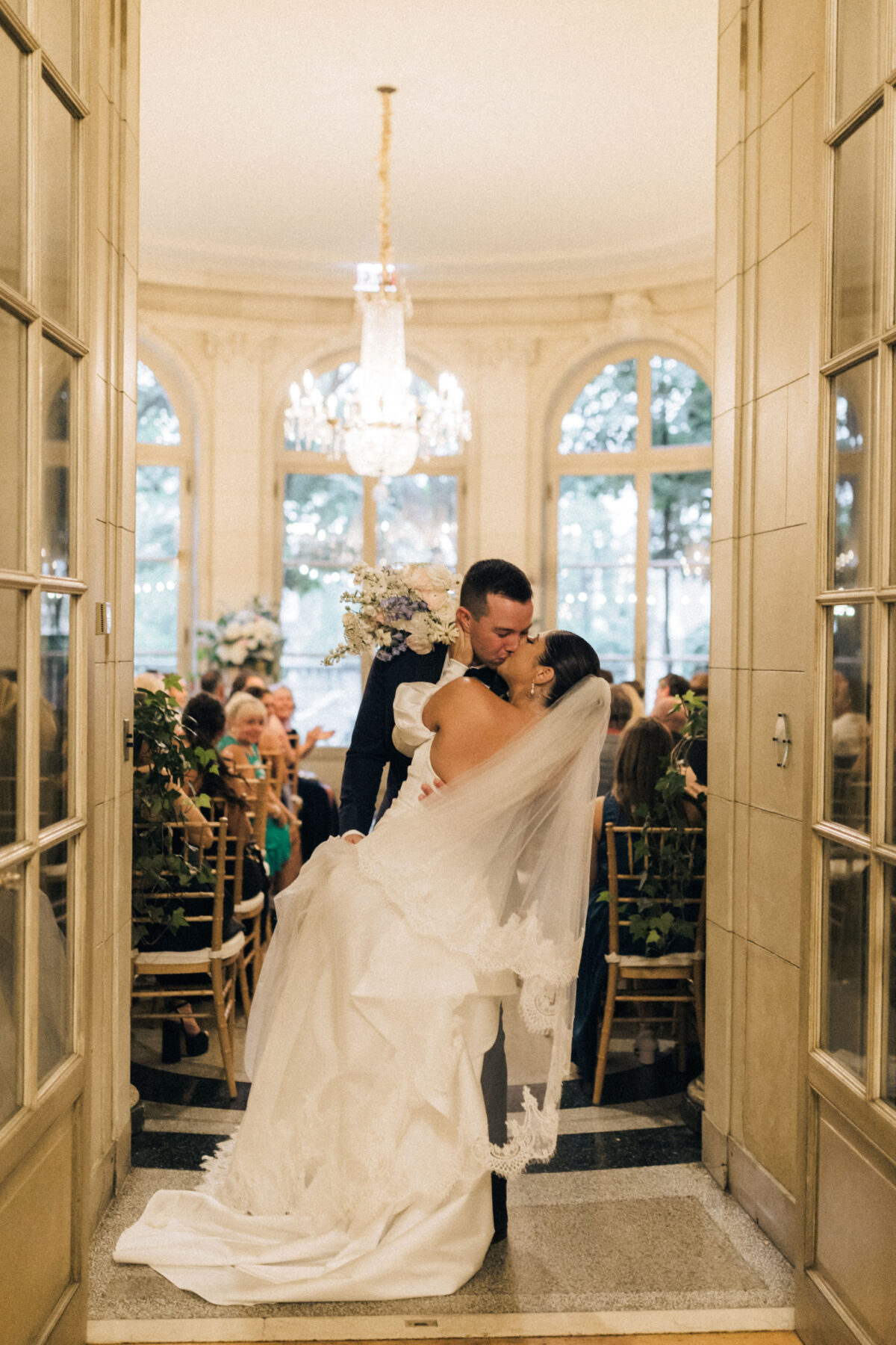 Bride and groom share a romantic dip and kiss at their Meridian House garden wedding in Washington, D.C., framed by French doors and chandeliers. Planned by a full-service DC wedding planner.