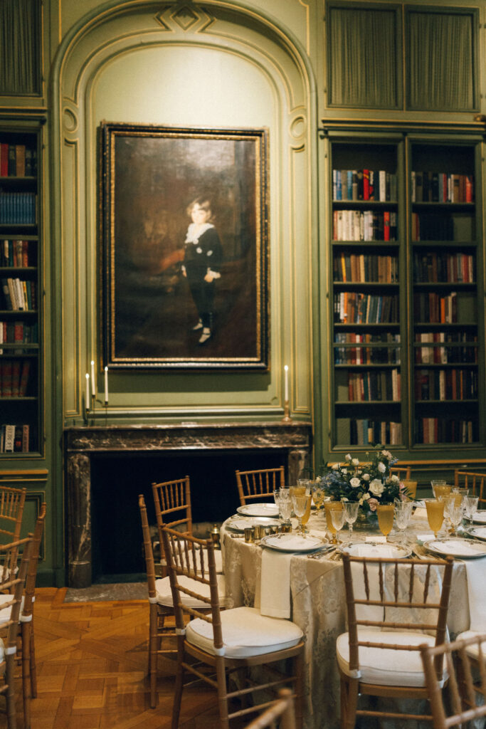 Reception table set beneath a vintage portrait and fireplace in the Meridian House library, surrounded by ornate bookshelves. Fall wedding Meridian House Washington DC. 