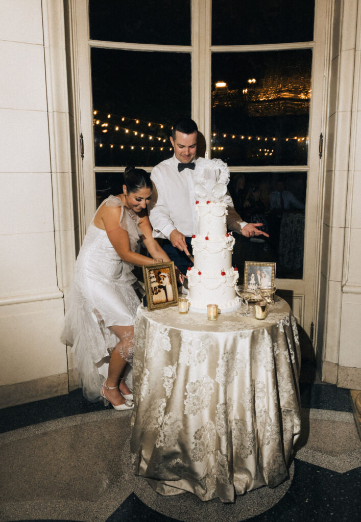 Bride and groom cutting their retro-tiered wedding cake inside Meridian House, surrounded by vintage family photos and candlelight.