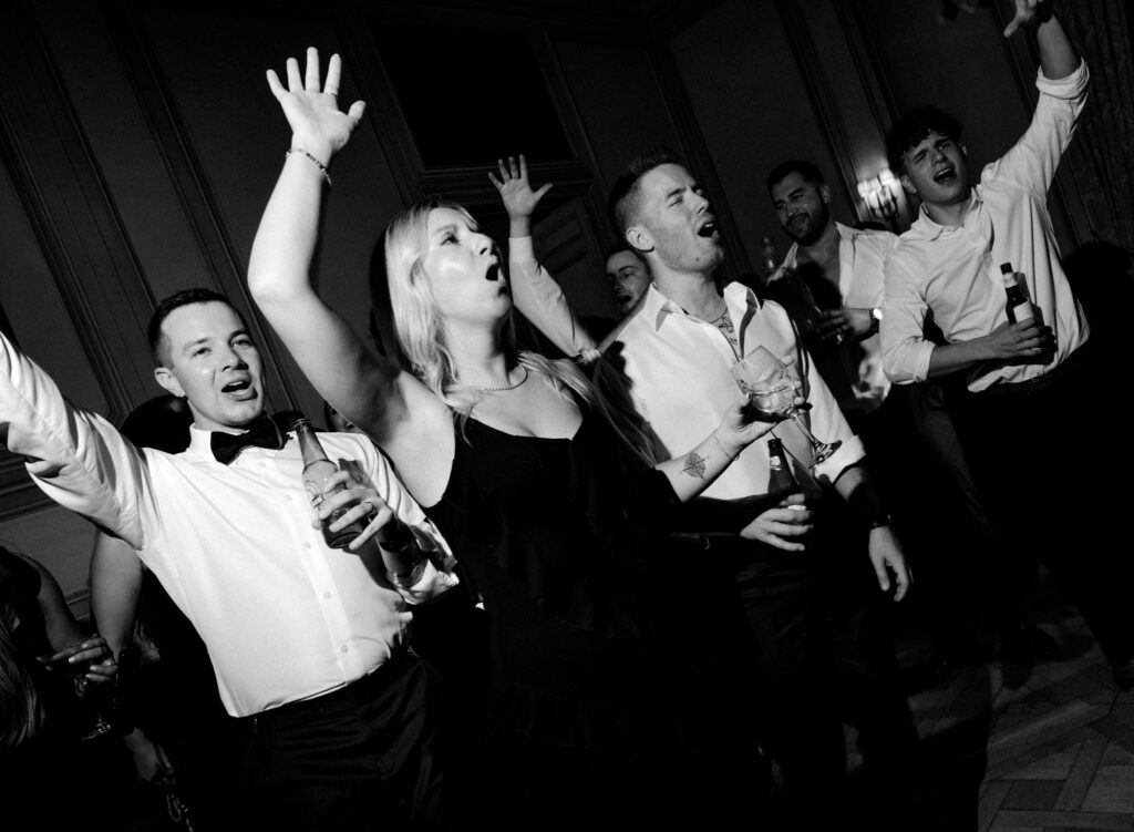 Black and white photo of wedding guests singing and cheering together on the dance floor at Meridian House.