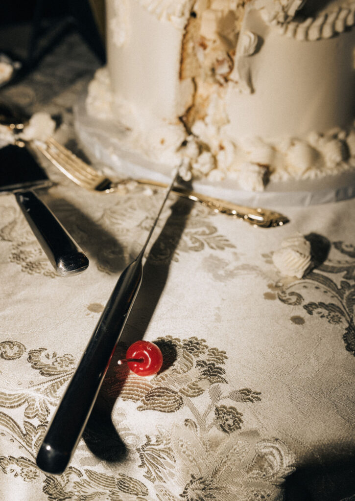 Close-up of a sliced wedding cake with a maraschino cherry and vintage utensils on brocade linen at Meridian House in D.C. Anti Bride