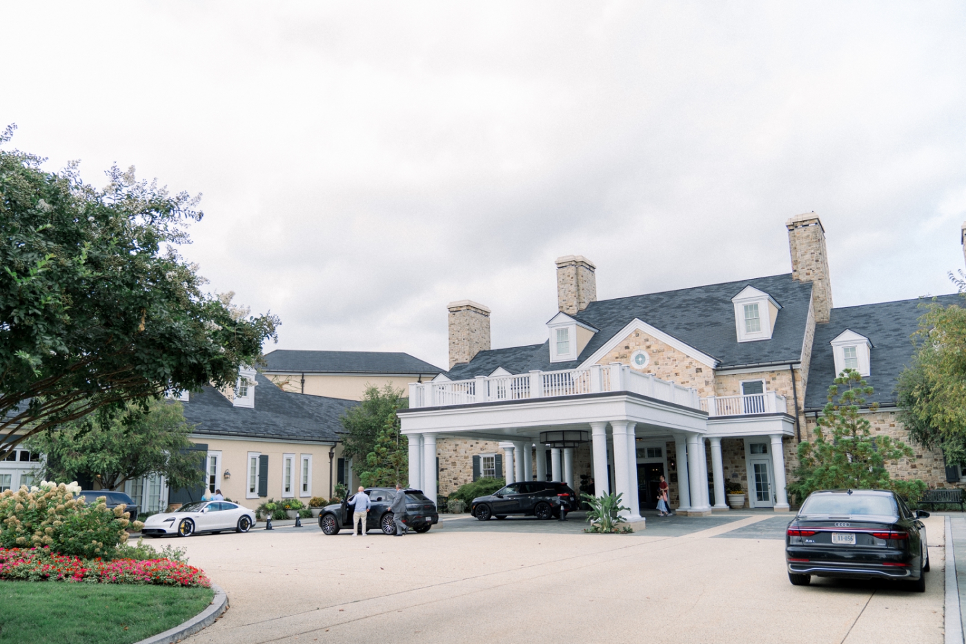 A large yellow buidling with a large driveway with multiple cars in line beneath an awning