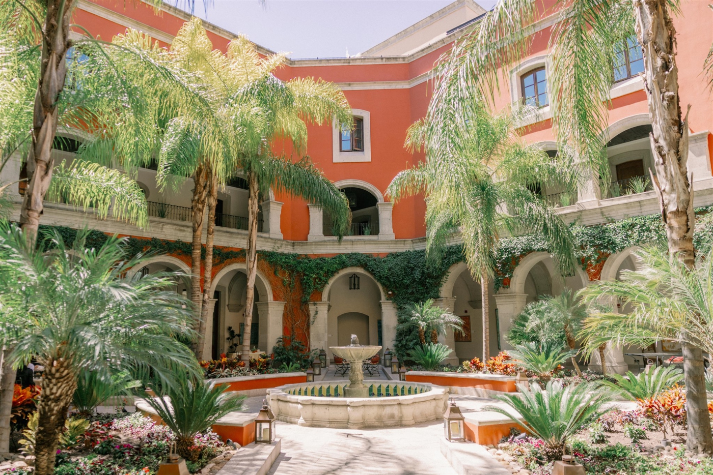 A terracotta colored courtyard surrounded by palm trees with a fountain in the center at a hotel in San Miguel