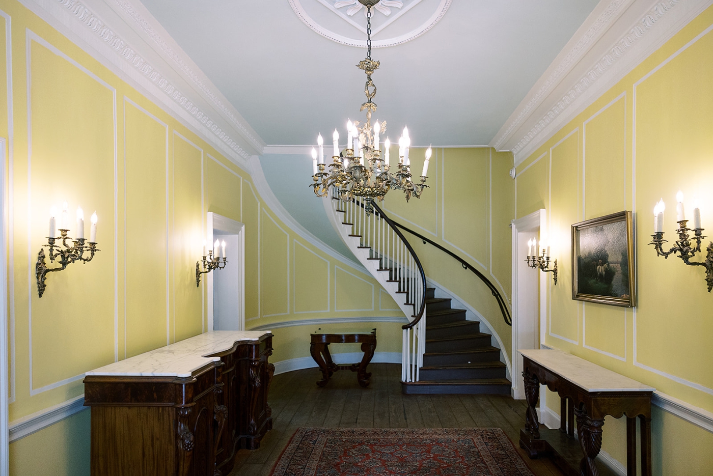 A large spiral staircase in a pastel yellow entryway at Lowndes Grove