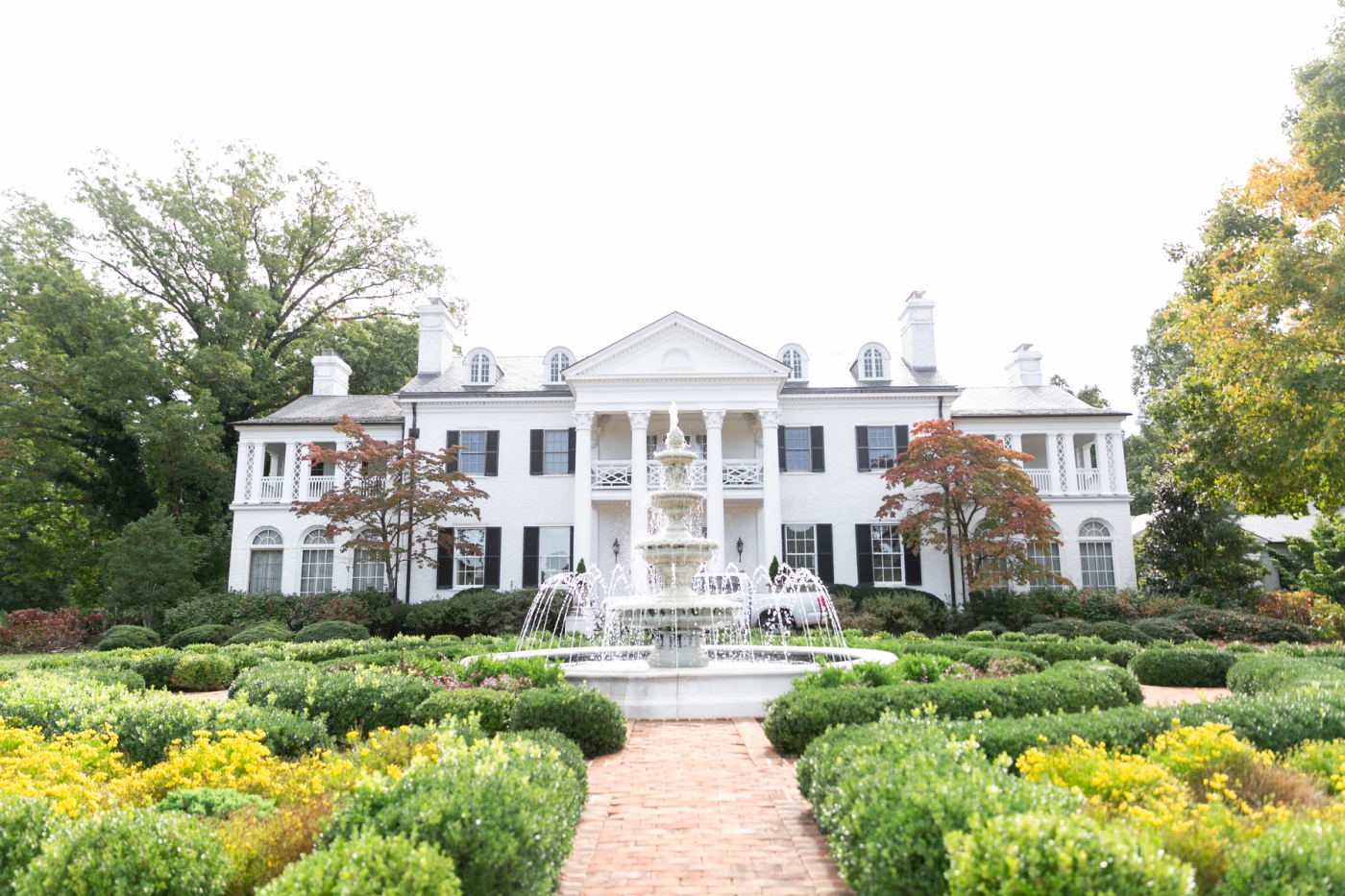 A sprawling white mansion surrounded by manicured gardens and hedges