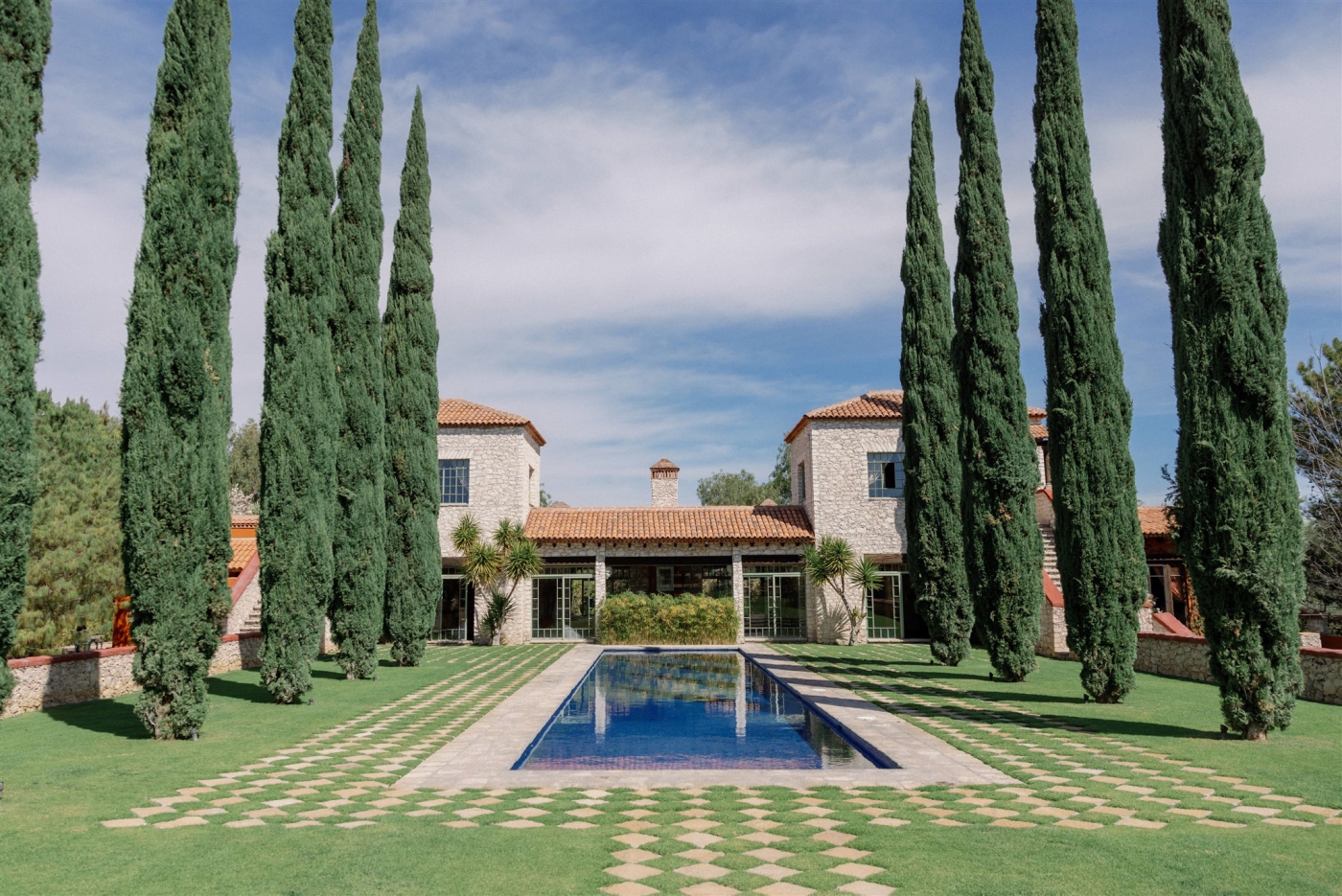 A long, thin blue pool surrounded by tall Mediterranean cypress trees